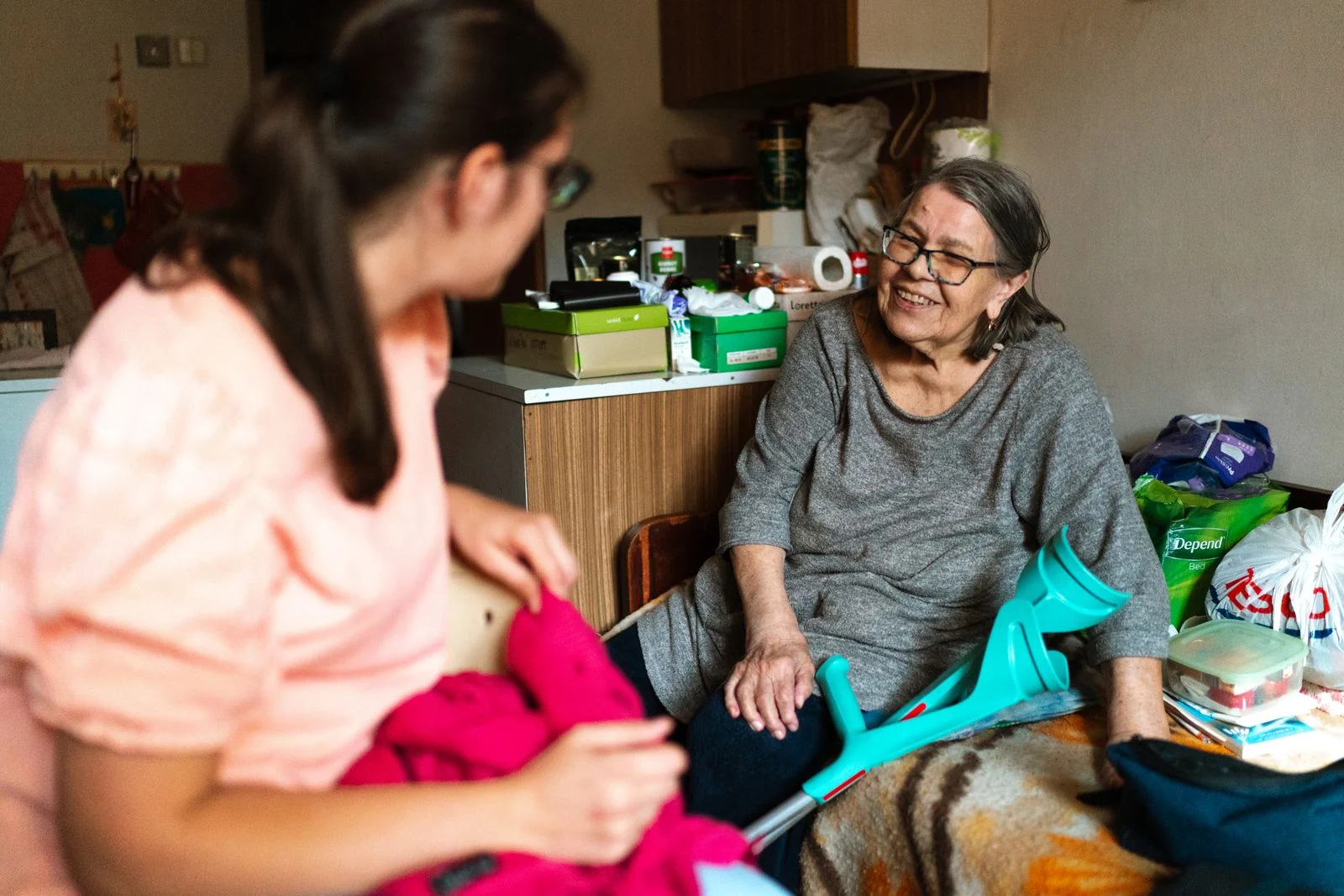 Mujer mayor sonriente en su casa conversando con una familiar más joven que la ayuda